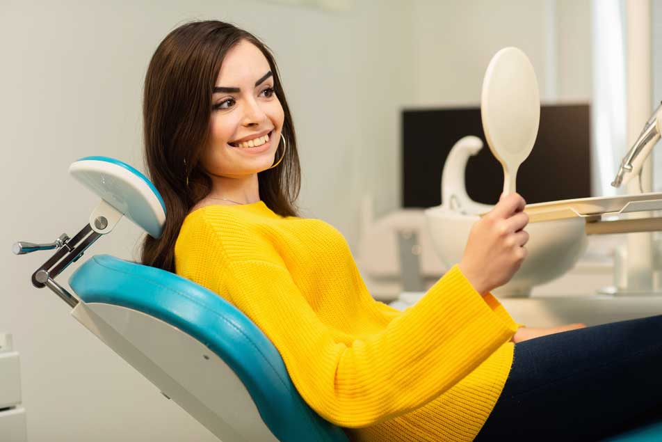 Девушка сидит в стоматологическом кресле и смотрит в зеркало