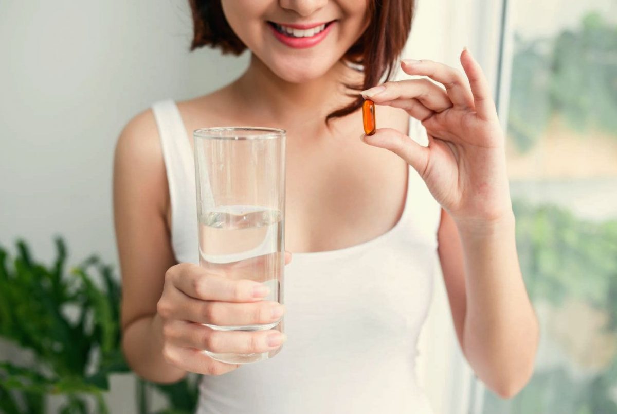 Девушка пьет витамины запивая стаканом воды